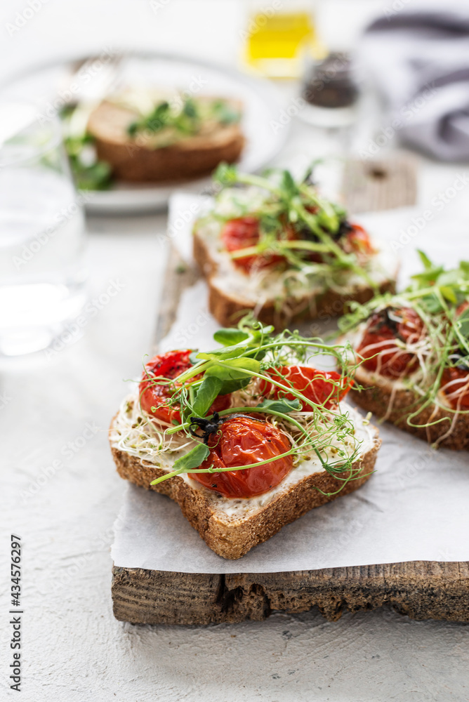 Healthy sandwich with cream cheese, baked tomatoes and micro greens on white background. Healthy breakfast sandwiches on a wooden board