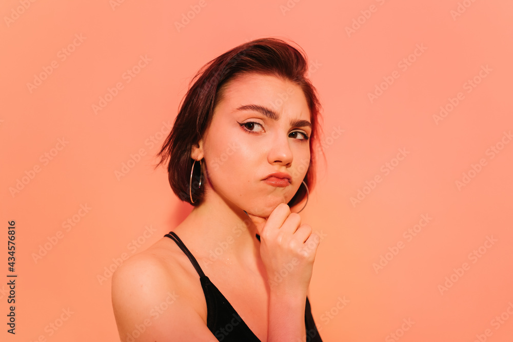 thoughtful young woman looking away with hand near face on orange background