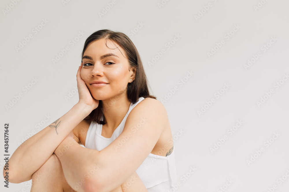 smiling young woman hugging knees with hand near face and arms crossed isolated on grey smiling young woman hugging knees with hand near face and arms crossed isolated on grey