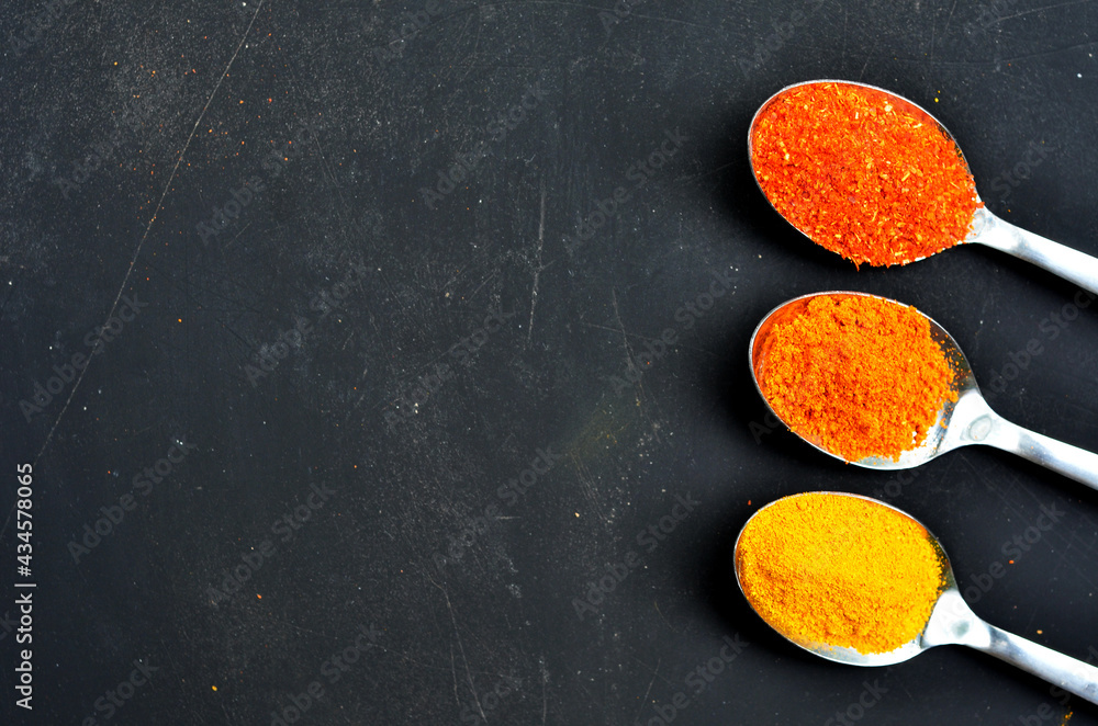 various colors of spices in a spoon on a black background. curry powder, turmeric, chilies. top view with selective focus various colors of spices in a spoon on a black background. curry powder, turmeric, chilies. top view with selective focus
