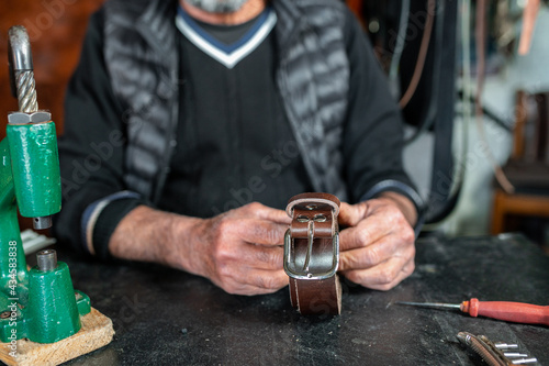 Cropped artisan senior man looking at he camera and showing his work, a leather strap.