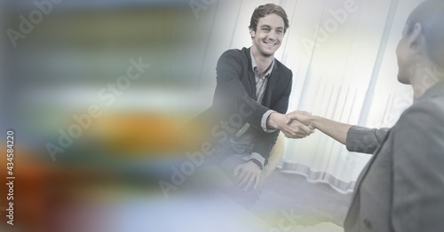 Composition of smiling businessman and businesswoman shaking hands in meeting room with motion blur