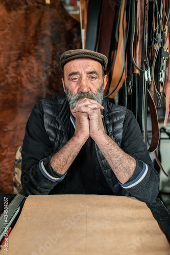 Vertical portrait of senior man looking at the camera. Sitting i workplace making products with genuine leather.