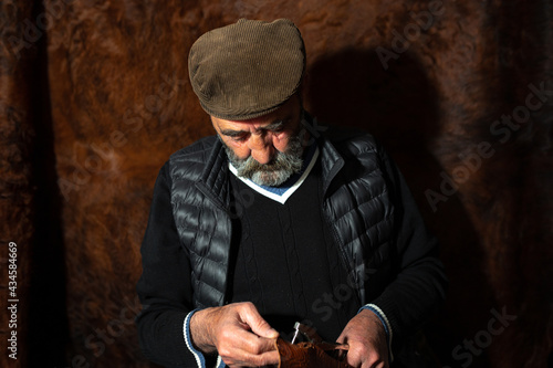 close-up of old leather craftsman working with skin an holding a tool