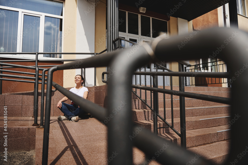 View through the railing of a young woman sitting on skateboard in lotus pose and having rest on a warm sunny day View through the railing of a young woman sitting on skateboard in lotus pose and having rest on a warm sunny day