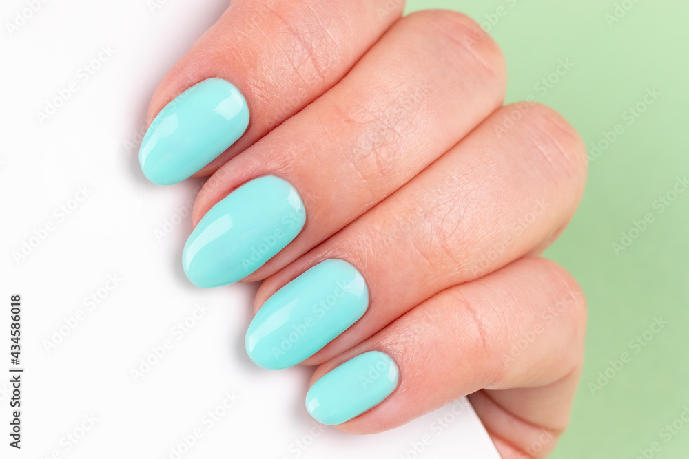 Female hand with beautiful manicure - mint blue nails with white smartphone on green background, closeup. Selective focus Female hand with beautiful manicure - mint blue nails with white smartphone on green background, closeup. Selective focus
