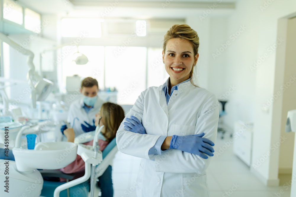 Dentist female with crossed arms wearing white coat posing and looking at camera. Dentist female with crossed arms wearing white coat posing and looking at camera.