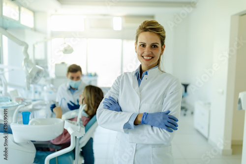 Dentist female with crossed arms wearing white coat posing and looking at camera.