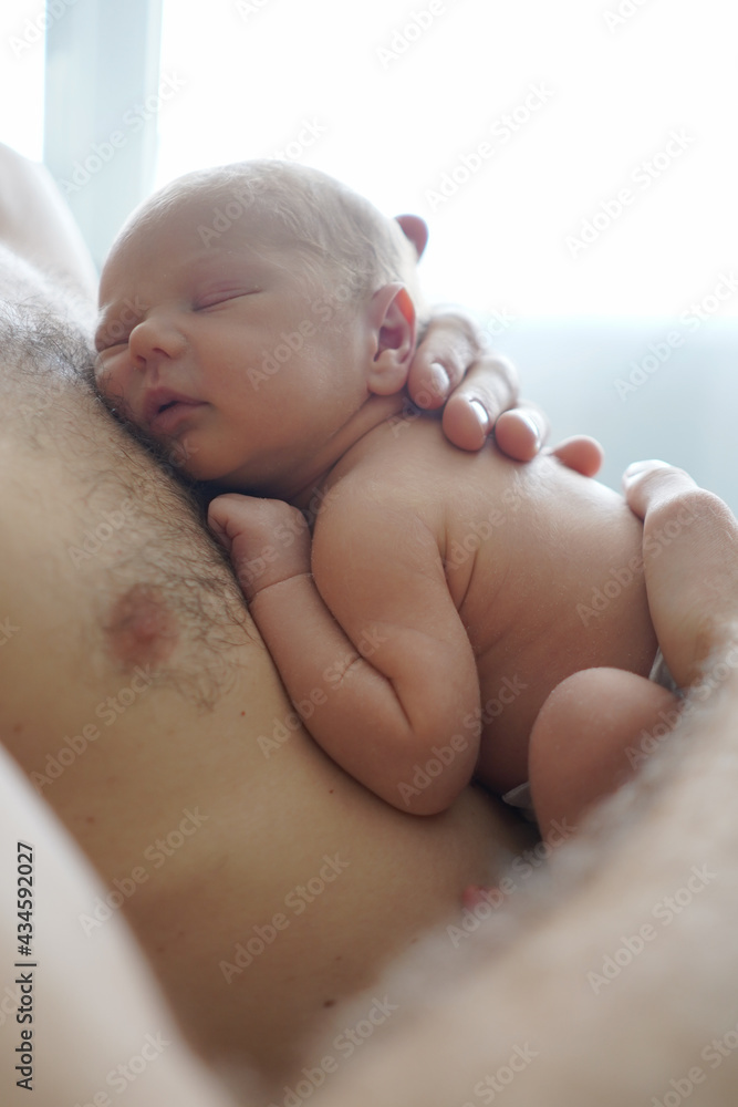 Side view of crop anonymous father with naked torso tenderly embracing adorable sleeping infant
