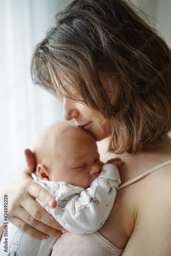 Side view of loving mother gently embracing and kissing adorable sleeping baby at home