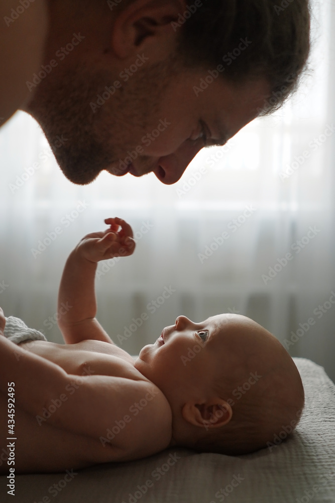 Side view of crop smiling father looking at cute infant lying on bed at home