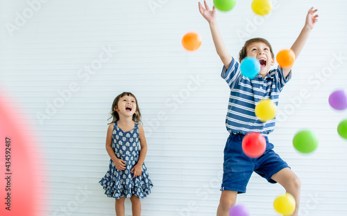 Caucasian little adorable sibling boy and girl laughing, screaming, celebrating birthday party, playing colorful balls together with happiness and playfulness. Education, Family Concept.