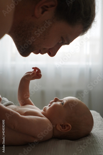 Obraz na płótnie Side view of crop smiling father looking at cute infant lying on bed at home w salonie