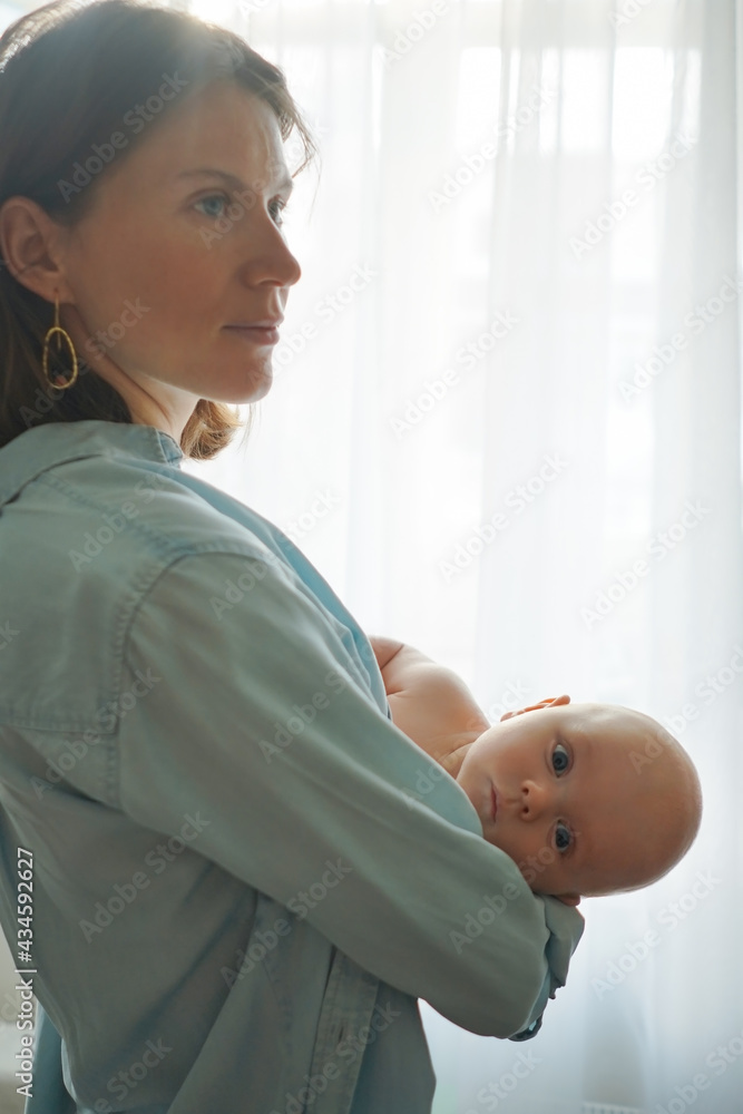 Side view of loving mother standing with adorable infant in room at home