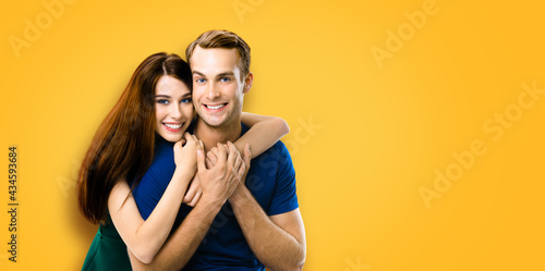 Smiling attractive young amorous couple. Portrait of embracing caucasian models at happy in love studio concept, isolated on orange yellow color background. Man and woman posing together.