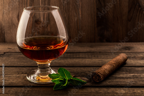 Glass of brandy with mint sprig and cuban cigar on an old wooden table