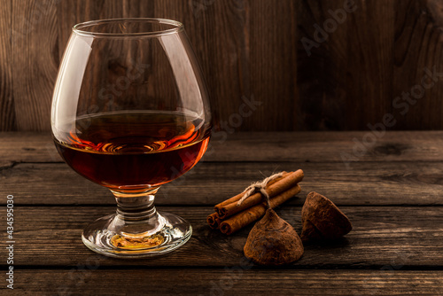 Glass of brandy and a couple of chocolate truffles with cinnamon sticks tied with jute rope on an old wooden table. Focus on the chocolate truffles