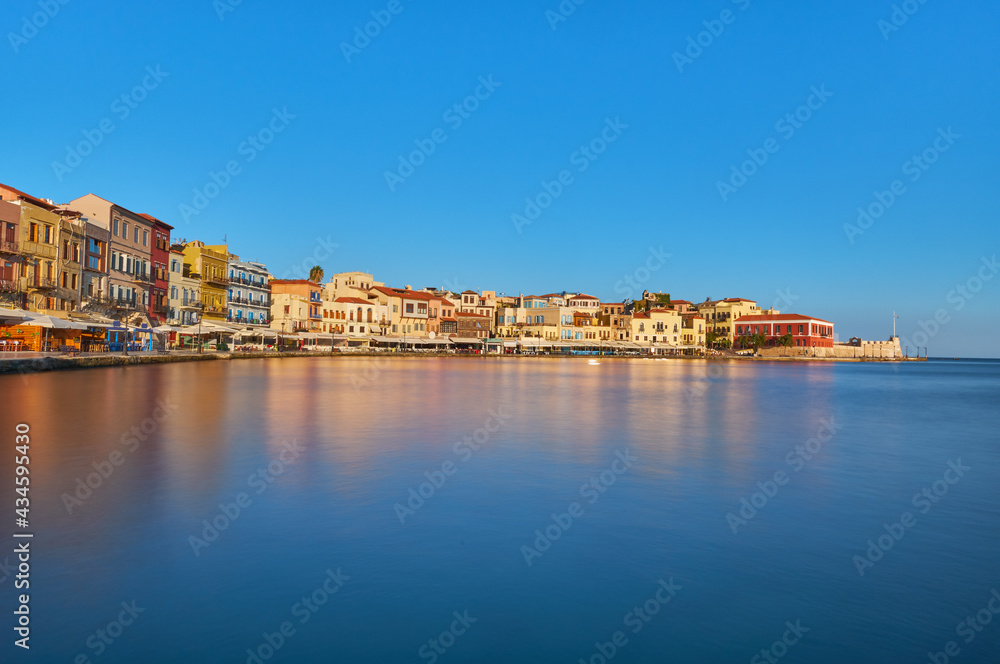 View of old port of Chania of Crete island Greece. Restaurants on the quay in the morning sun with reflections in the polished water in the foreground. Bay of Xania at sunny summer day. The harbour of