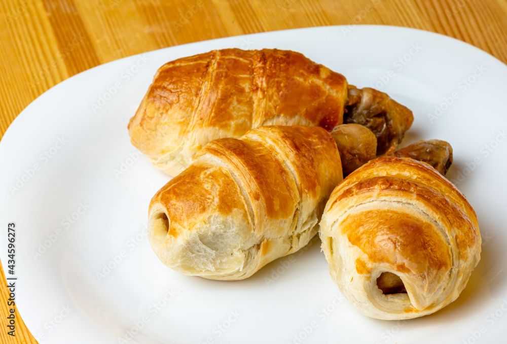 Appetizing chicken legs in puff pastry on a white plate and wooden background Appetizing chicken legs in puff pastry on a white plate and wooden background