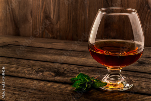 Glass of brandy with mint sprig on an old wooden table. Angle view