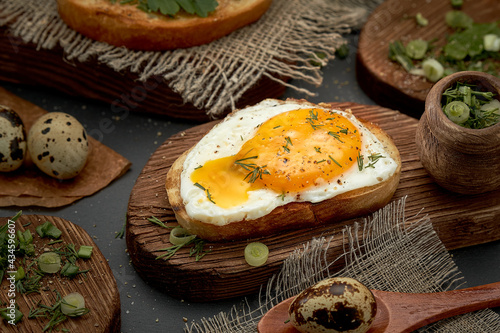 Fried eggs on a bun with black pepper and herbs on a wooden board. The scrambled eggs are spreading.