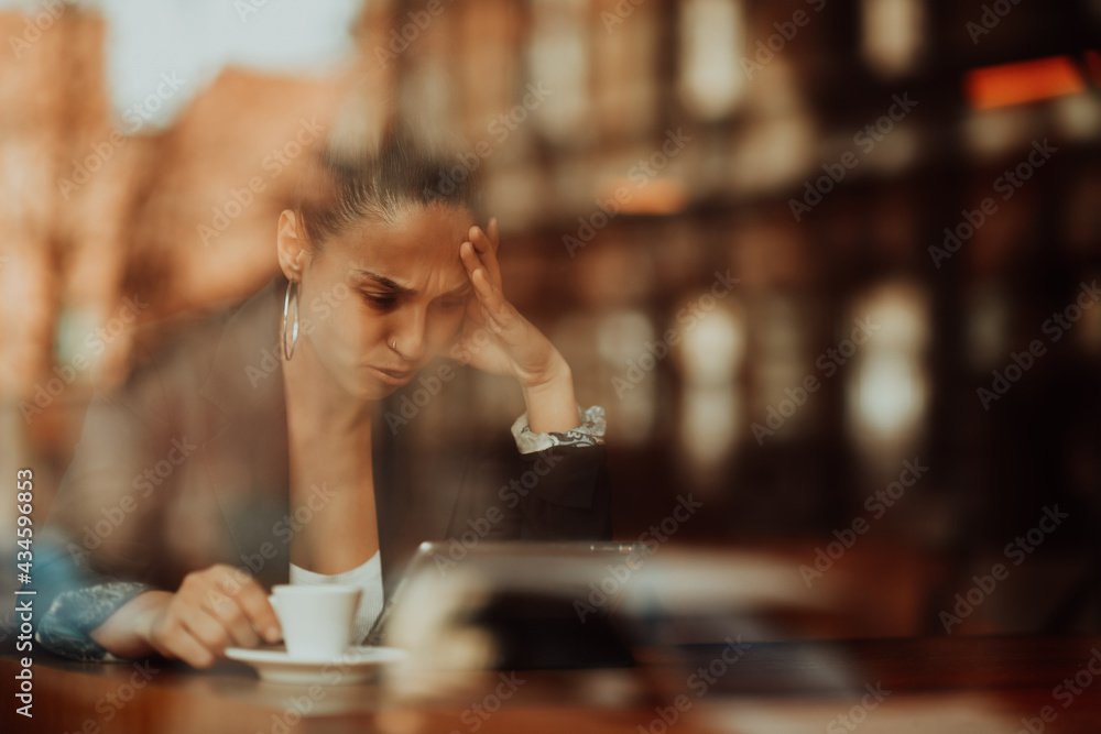 A Latin woman sits in a café looking anxiously at a tablet A Latin woman sits in a café looking anxiously at a tablet