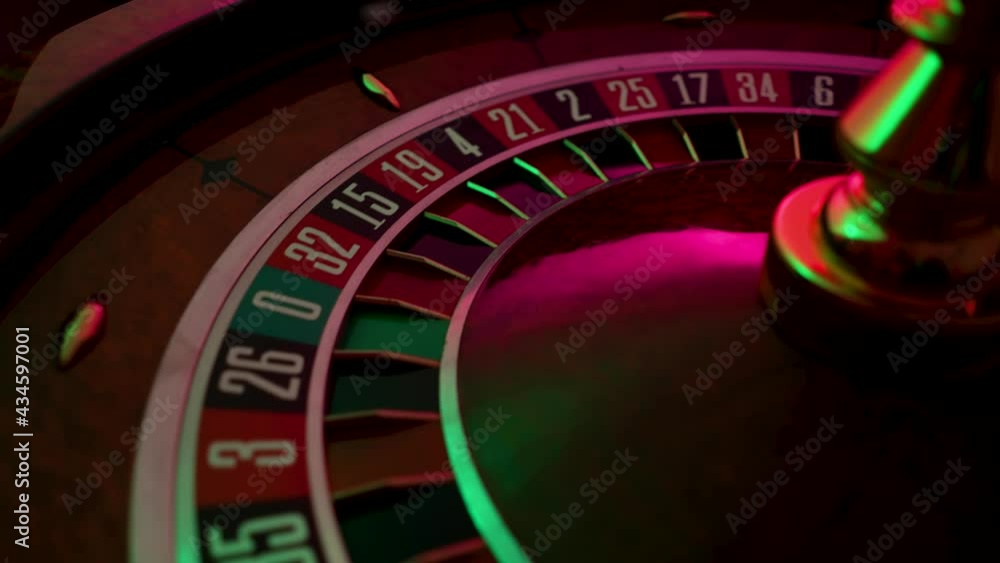Rotating roulette wheel close up in the rays of purple neon lights. The small white ball hits red 14, the bet wins. Part of the roulette wheel runs in slow motion. Rotating roulette wheel close up in the rays of purple neon lights. The small white ball hits red 14, the bet wins. Part of the roulette wheel runs in slow motion.