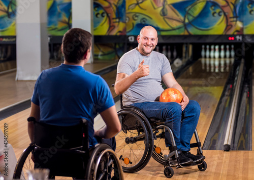 Two young disabled men in wheelchairs playing bowling in the club