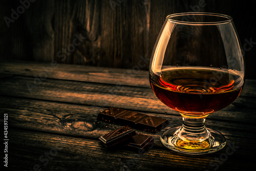 Glass of brandy and a chocolate on an old wooden table. Angle view
