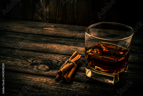 Glass of brandy with cinnamon sticks tied with jute rope on an old wooden table. Angle view