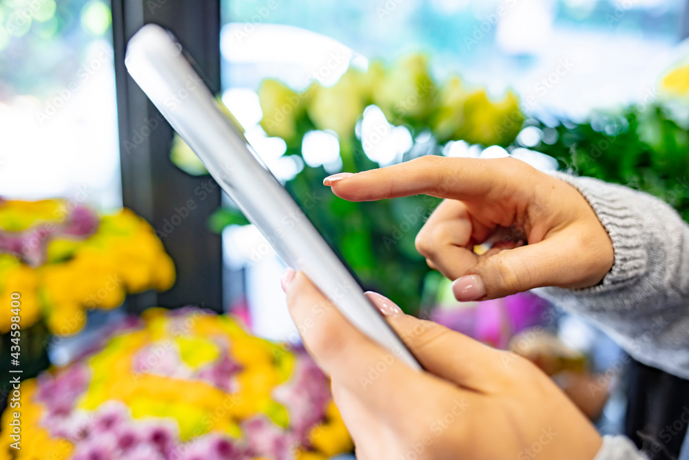 Mid section portrait of unrecognizable florist using digital tablet in shop.  Young female florist standing in her flower shop checking online orders with a digital tablet