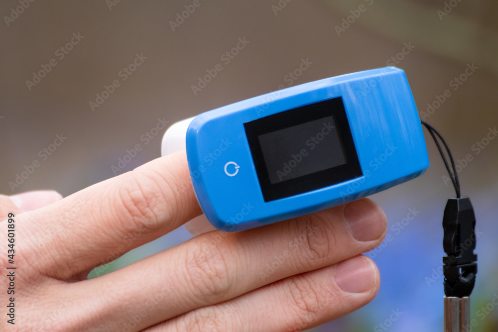 Pulse oximeter on a finger. Blue oxygen saturation meter (SPO2). Device outdoors close-up with spring blue scilla flowers and selective focus blur background Pulse oximeter on a finger. Blue oxygen saturation meter (SPO2). Device outdoors close-up with spring blue scilla flowers and selective focus blur background