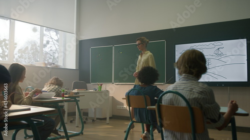 Students sitting at desks in classroom. Teacher explaining lesson to pupils