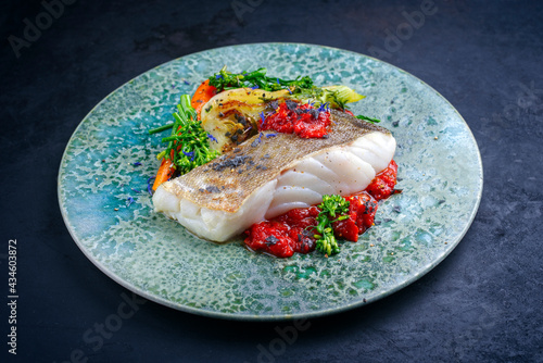 Modern style traditional fried skrei cod fish filet with fennel and tomato cream served as close-up on Nordic design plate with copy space