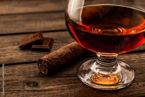 Glass of brandy and a chocolate with cuban cigar on an old wooden table. . Close up view, shallow depth of field