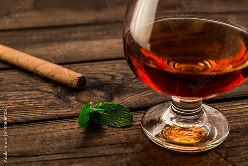 Glass of brandy with mint sprig and cuban cigar on an old wooden table. Close up view, shallow depth of field