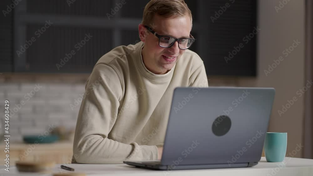 Smiling young male communicating by video live using computer, video conference. Young male taking notes when communicating on video link Smiling young male communicating by video live using computer, video conference. Young male taking notes when communicating on video link