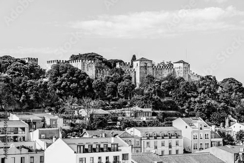 The castle of Saint George (Sao Jorge), fortified medieval walls beyownd houses roof tops and trees in Lisbon, Portugal in black and white