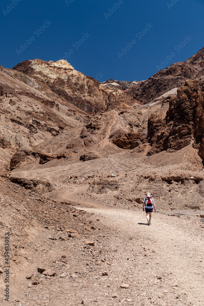 A lone hiker treks through the blazing sun toward Natural Bridge in Death Valley National Park, California
