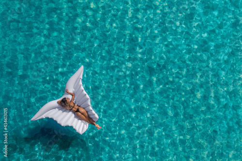 Aerial view of young tanned woman swimming on the inflatable wings in the transparent turquoise sea. Top view of slim lady relaxing on her holidays. © stryjek