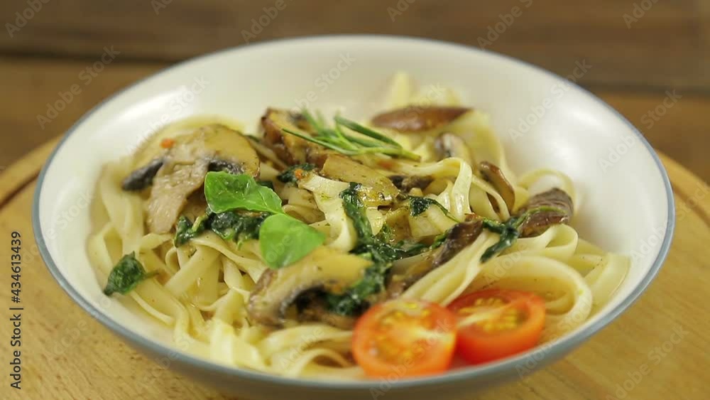 Udon with mushrooms and spinach and cherry tomatoes in a plate rotates in a circle Udon with mushrooms and spinach and cherry tomatoes in a plate rotates in a circle