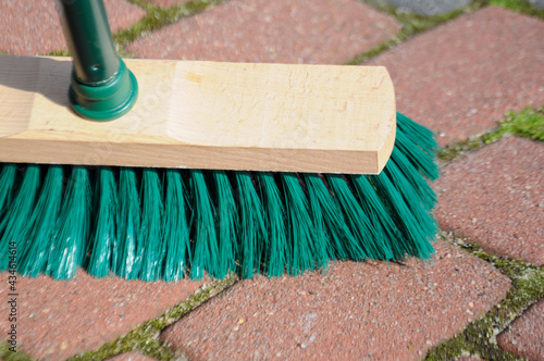 Green wooden brush while sweeping the bricky pavement outside photo