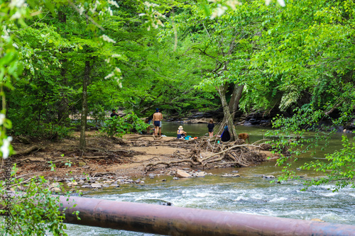 people relaxing on the banks of the Big Creek river surrounded by gorgeous lush green trees and water rushing down the river at Vickery Creek in Roswell Georgia photo