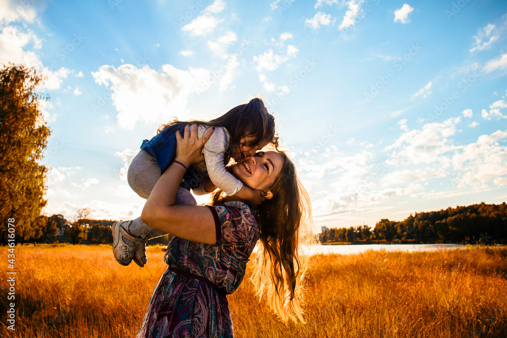 happy mother with a little daughter, having fun in nature, in the rays of the sunset