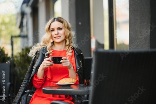 Fashion portrait of young woman siting at the table with cup of coffee, tea in street cafe.
