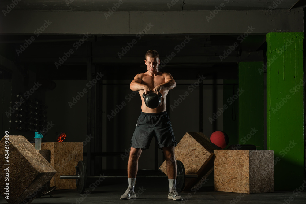 Naklejka premium Full-length photo of a handsome man with a naked torso exercising with a kettlebell on a dark background