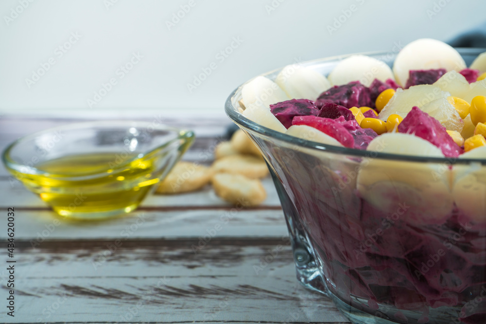 Beet, pineapple, corn, palm hearts and chicory salad with olive oil and basil in a glass bowl on a rustic table in still life style. Fresh and healthy vegetables concept. Beet, pineapple, corn, palm hearts and chicory salad with olive oil and basil in a glass bowl on a rustic table in still life style. Fresh and healthy vegetables concept.