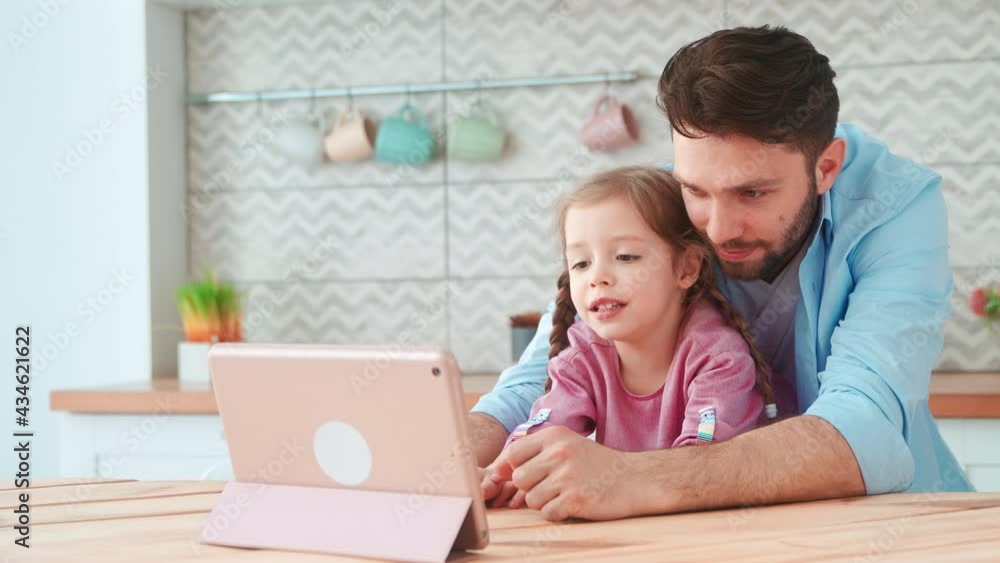 Young father and daughter looking cartoon on laptop. Smiling family in the kitchen Young father and daughter looking cartoon on laptop. Smiling family in the kitchen
