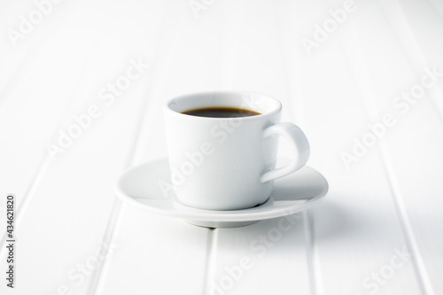 Black coffee in white mug on white wooden table.