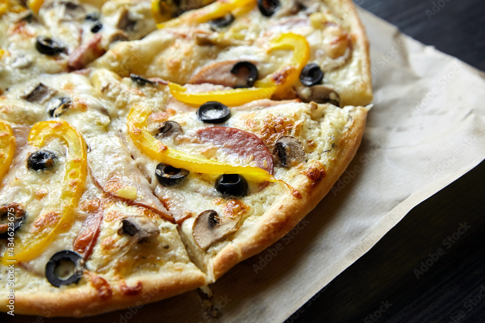 Pizza with chesse, ham, yellow bell pepper, olives and mushrooms on wooden table